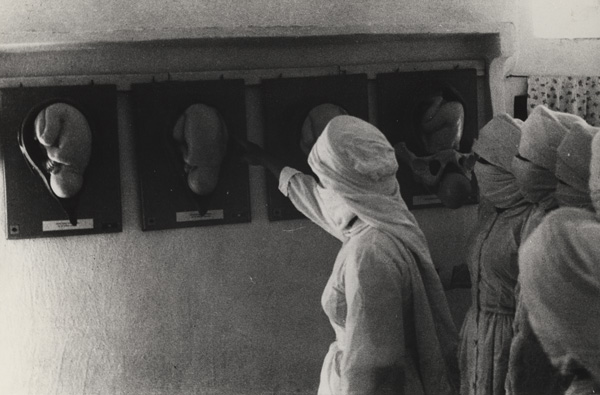 Three women in traditional Yemeni costume study images placed on a wall. 