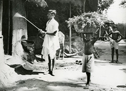 A man holds a spraying tool against an exterior wall, while two youths stand near.