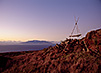 A wooden structure is pictured amidst a rust-colored landscape of scrubby brush and rockiness.