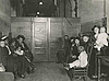 Waiting room filled with seated women and children, all looking at the viewer.