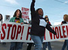 A woman holding a sign aloft leads other women holding banners and signs, marching down a street. 