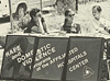 Four women sitting at a table with identifying sign.