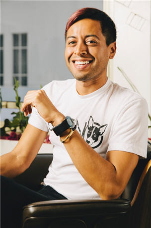 Young man seated in a chair smiles.