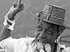 African American woman speaks in front of a bank of microphones to a crowd out of view to the left.