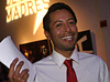 Latino man smiling holding several pieces of paper.