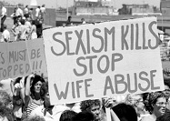 Crowd of people marching holding anti-domestic violence signs.