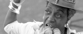 African American woman speaks in front of a bank of microphones.