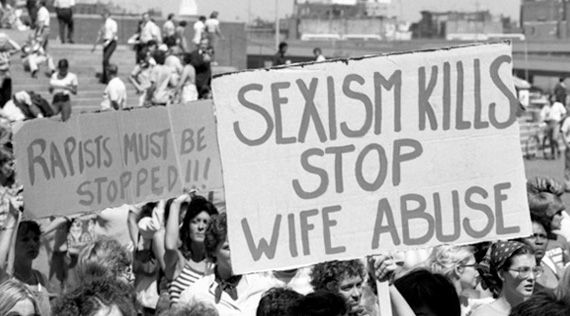 Crowd of people marching holding anti-domestic violence signs.