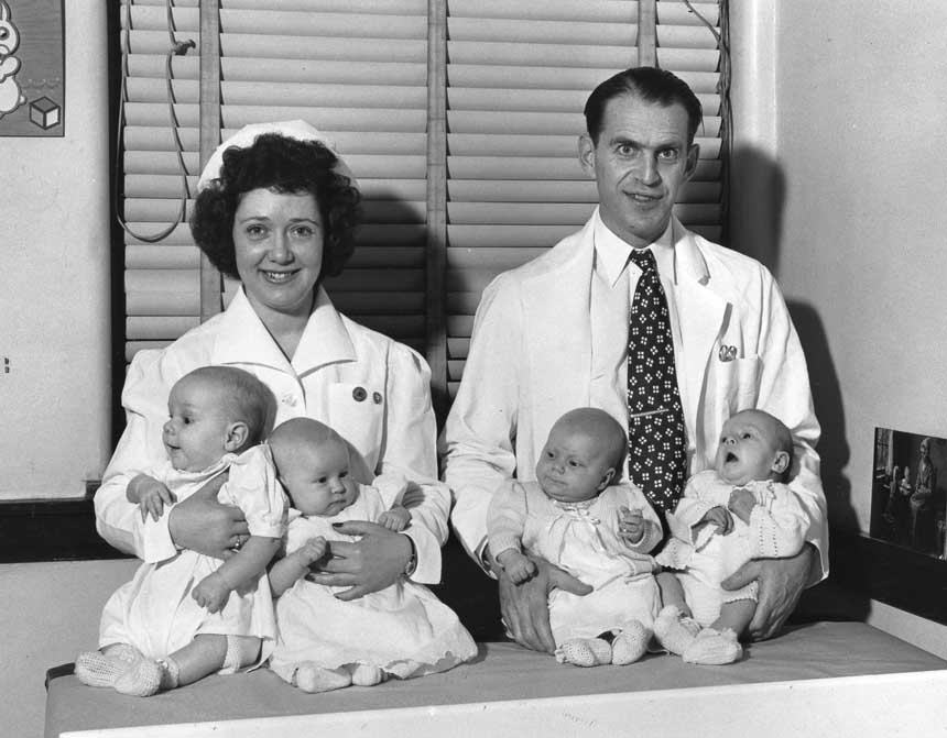 White male doctor and female nurse holding two White babies each and looking at viewer.