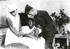 A wounded Choctaw soldier in the U.S. service lies in a bed while an army doctor and Red Cross nurse attend to his wounds. World War I, U.S. National Red Cross Hospital No. 5, Auteuil, France, circa 1917-1918. Image A011591 from Images from the History of Medicine (IHM).