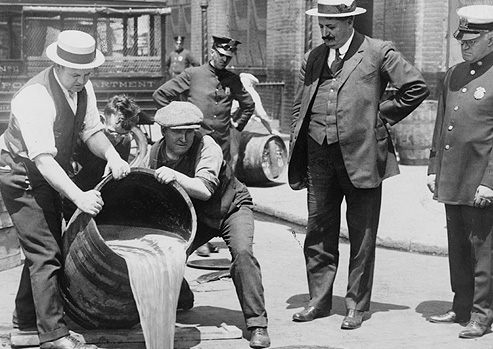 Black and white photograph of police officers overseeing the pouring out of alcohol.