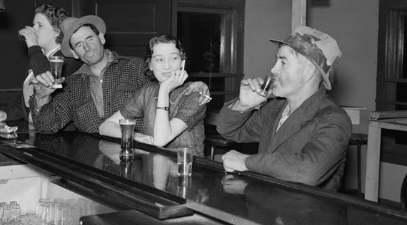 Black and white photograph of four people drinking alcohol at a bar.