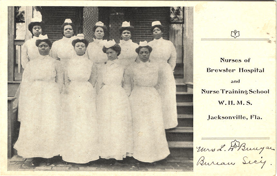 Nine African American female nurses in white standing in a group looking at the viewer.