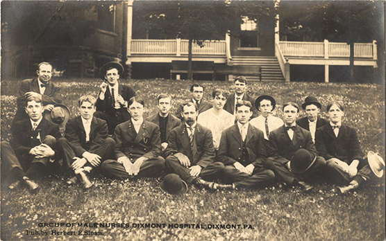 Fifteen White male nurses sitting in a group on a grass lawn.