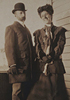 A woman and man standing on a porch in nice clothes, the woman is smiling.