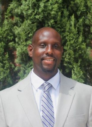 Photograph of a Black man outdoors wearing a gray suit and striped tie