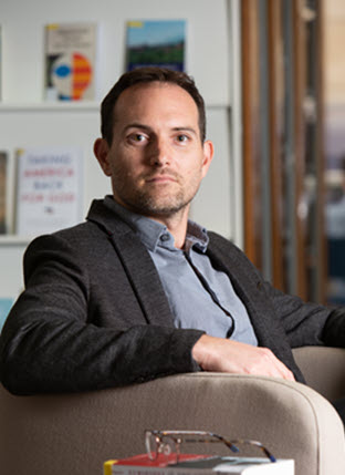 Photographic portrait of a white man in an office setting.