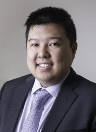 Photograph of an Asian man wearing a black suit and light-colored tie