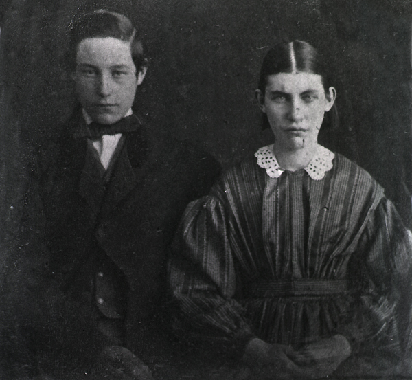 A young man on the left and a young woman on the right in formal, late 19th-century attire looking directly into the camera.